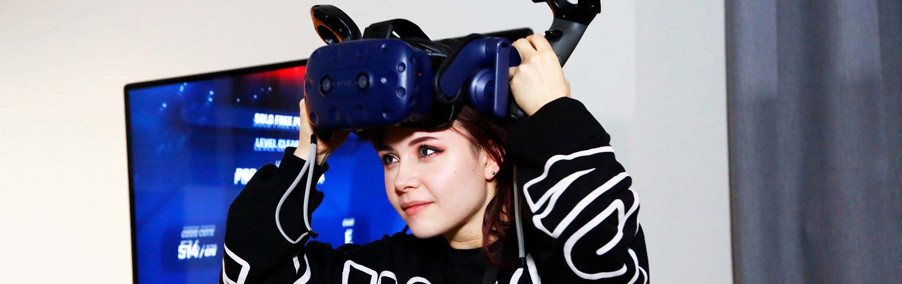 Kvinna med VR-set och spelet syns på skärm i bakgrunden