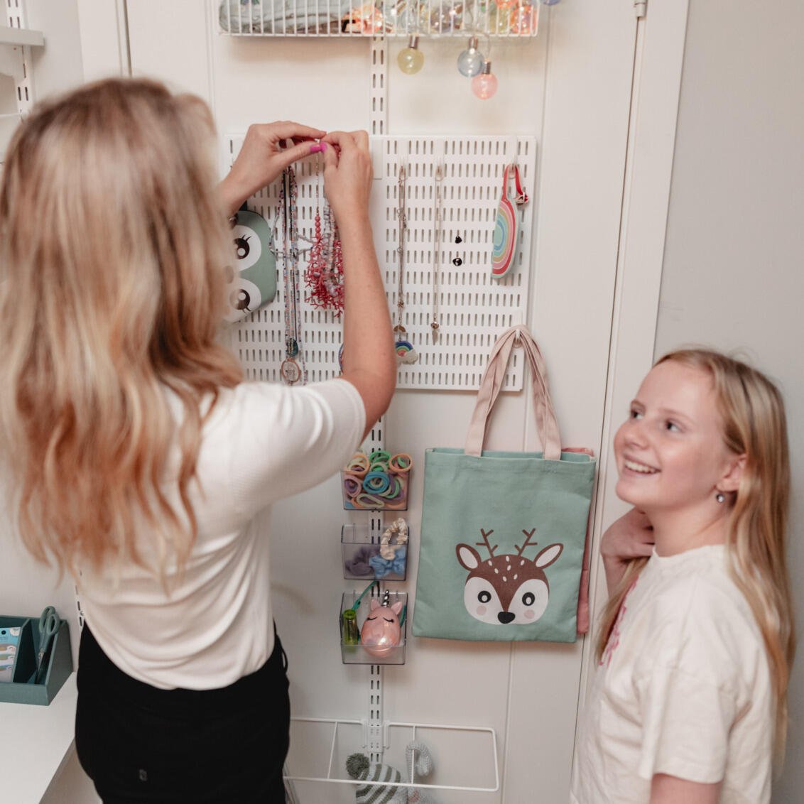 Jenny hänger ett halsband på dörrförvaringen från Elfa medan Vera tittar på.