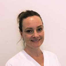 A woman in a white uniform smiles against a plain background.