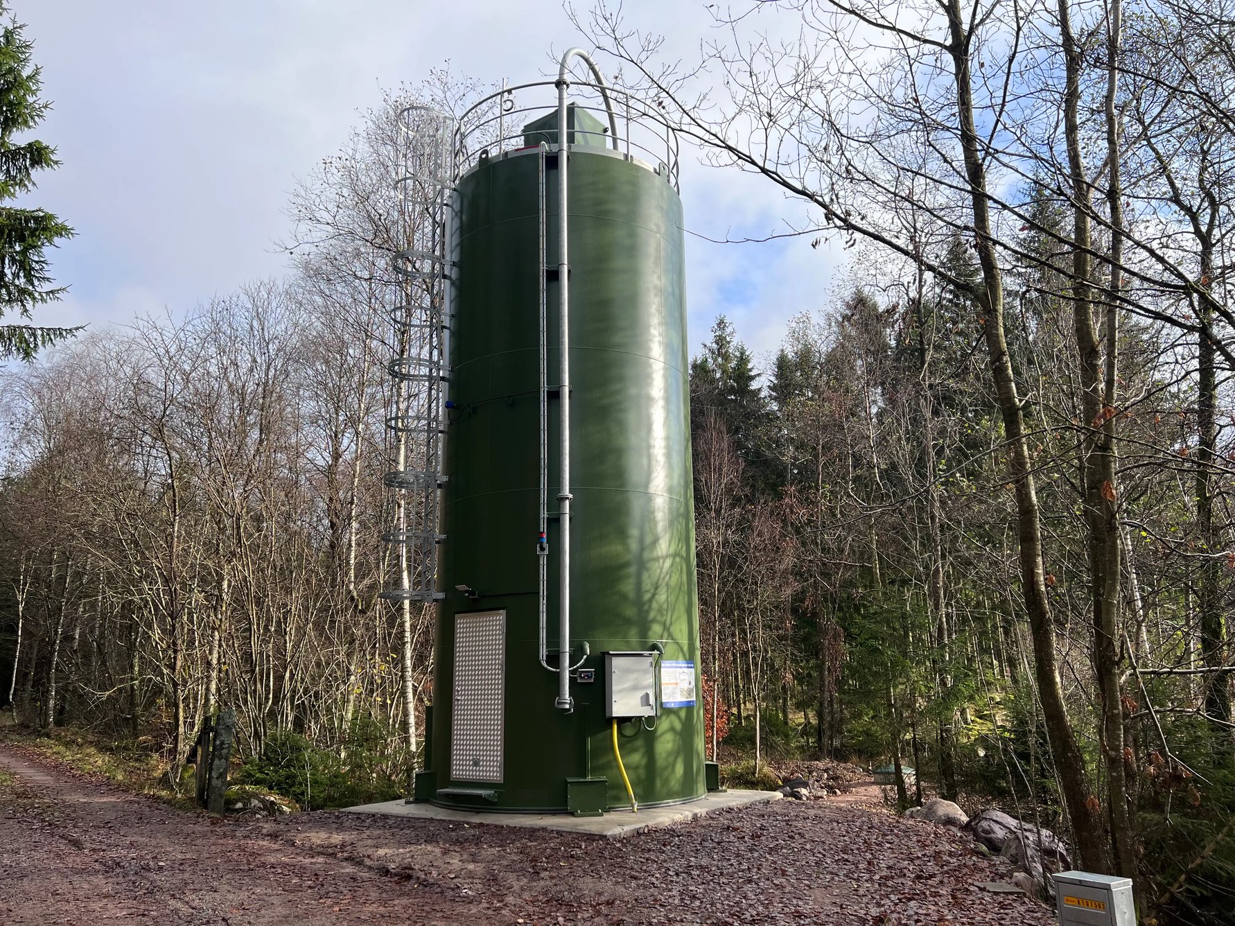 kalkdoserare - en stor grön cylinderformad behållare som står på betongplatta i skog vid vatten.